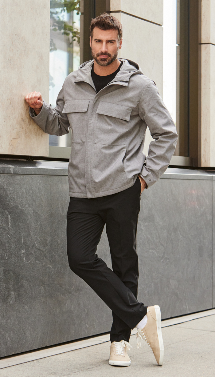 a man standing outside wearing a grey jacket and black pants